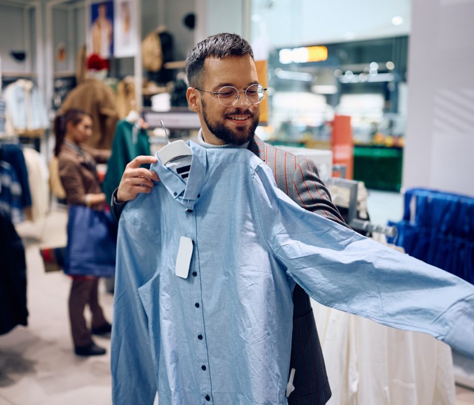 Happy man checking sleeve length while buying a shirt at shopping mall.